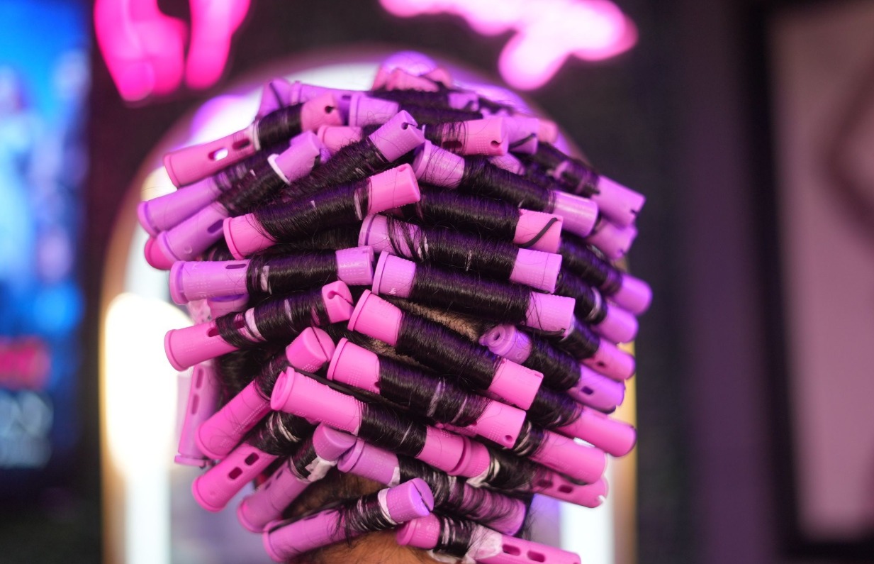 A full head of pink perm rods processing under the studio neon