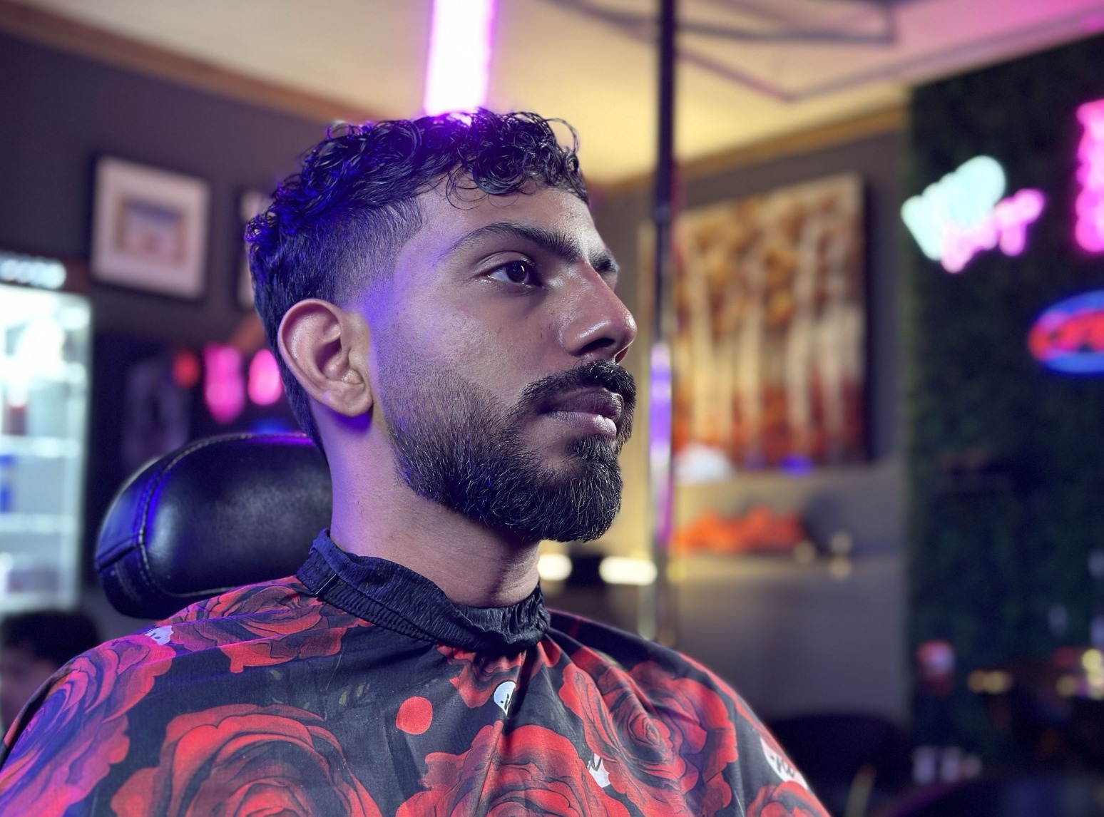 Client in the chair with a curly top, low taper and shaped beard