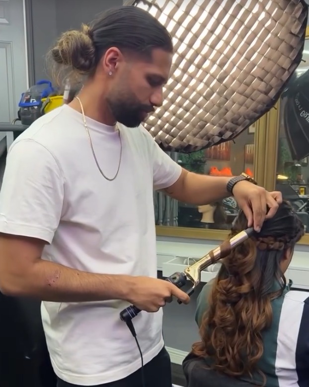 Vickram curling a client's long hair with a curling iron